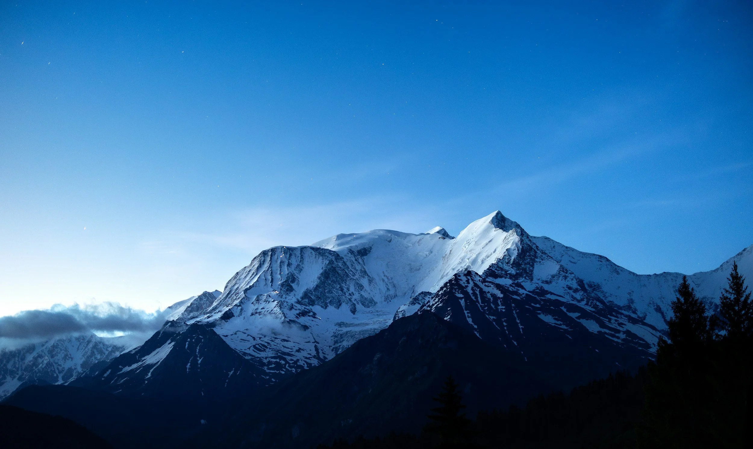 Snow-capped mountains under a clear blue sky at dusk.