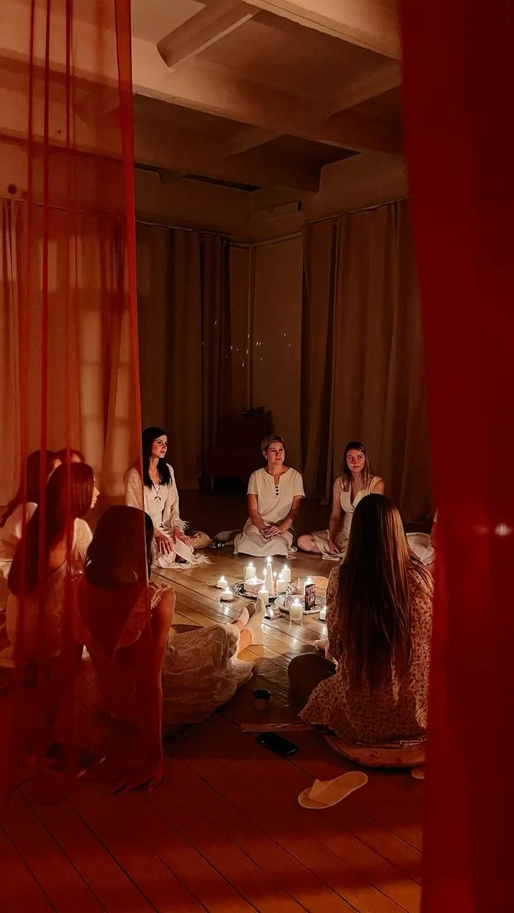 Groupe de femmes assises en cercle autour de bougies dans une pièce tamisée, ambiance paisible.