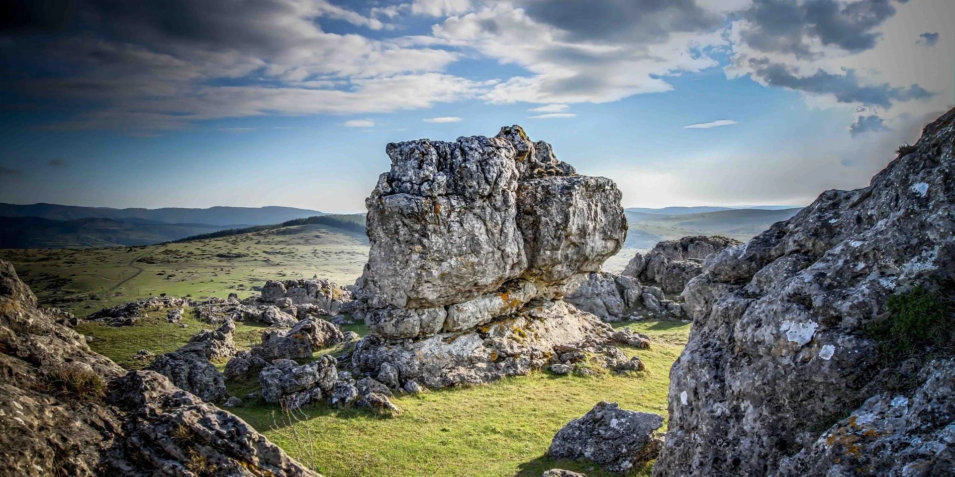 Grosses rocheau dans une plaine verdoyante avec d'autres rochers, fond de montagnes et ciel nuageux. lieu : Montpellier et alentours.