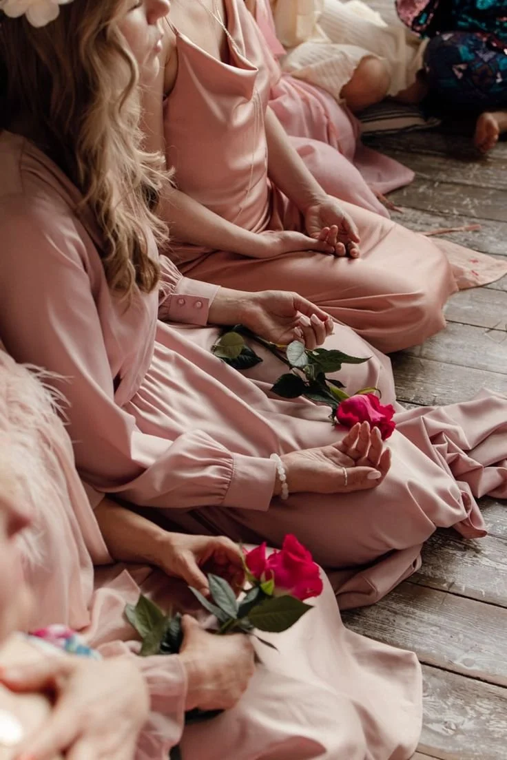 Femmes assises en cercle, portant des robes roses, tenant des roses roses dans leurs mains, assises sur un sol en bois.