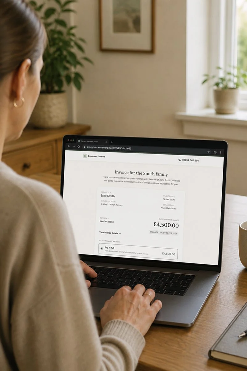 Person viewing an online funeral invoice on a laptop at a wooden table in a bright room with a window and houseplants.