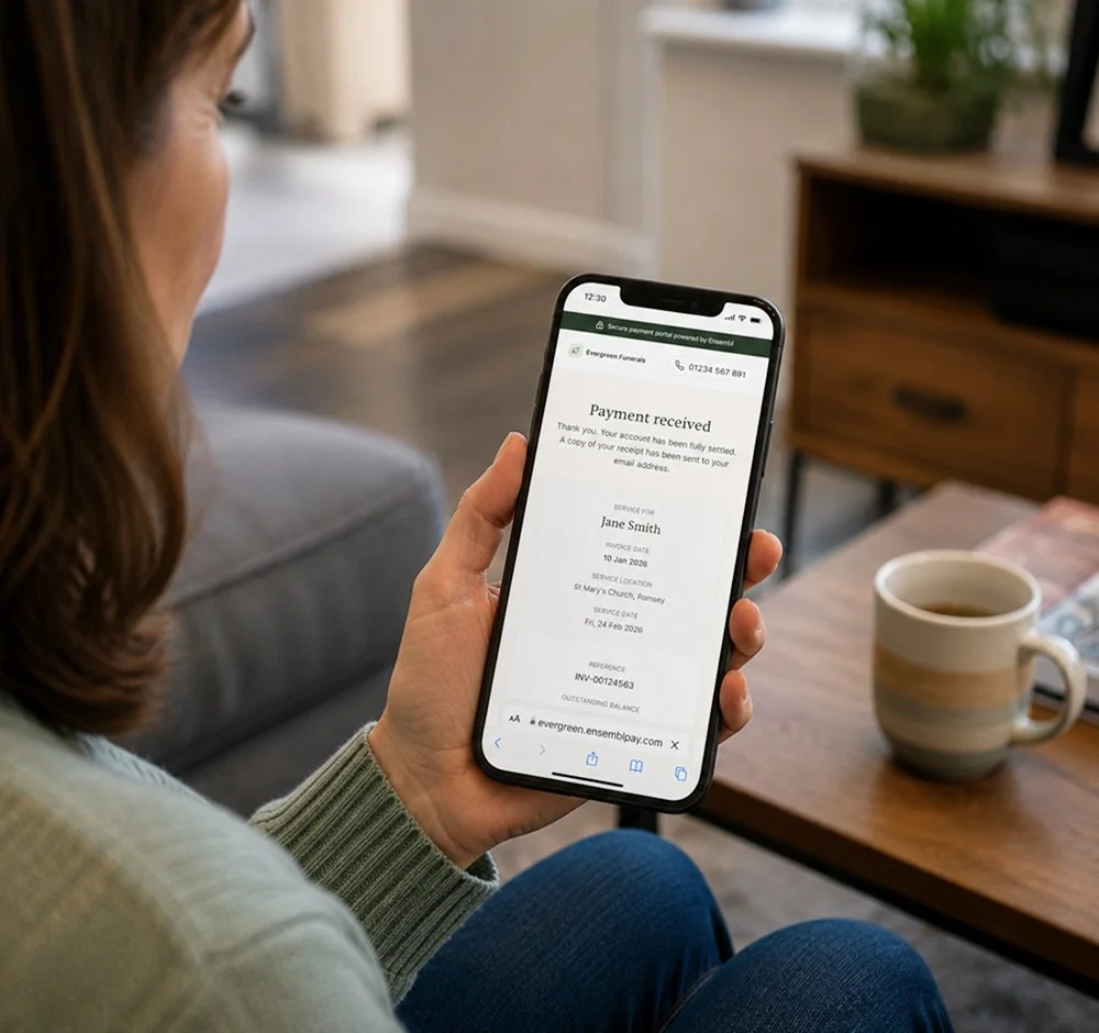 Woman sitting on a couch looking at her smartphone with a payment confirmation screen, coffee mug on a wooden table nearby.