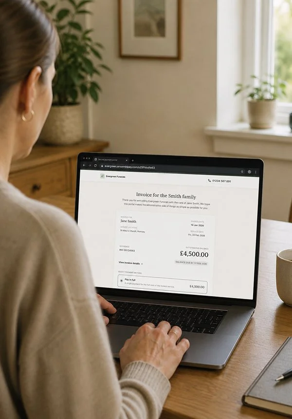 A person viewing an invoice for the Smith family on a laptop at a wooden table in a cozy room with natural light, a potted plant, and framed artwork.