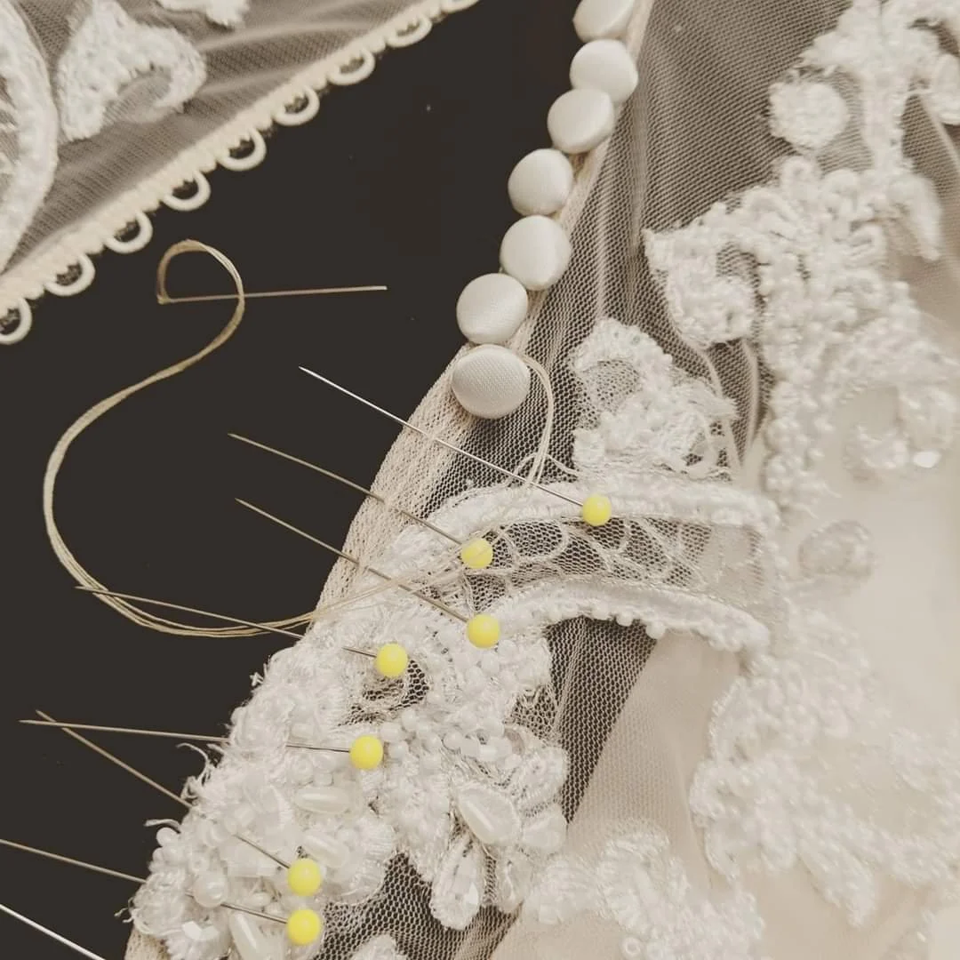 Close-up of embroidered lace fabric with pearls and pins.