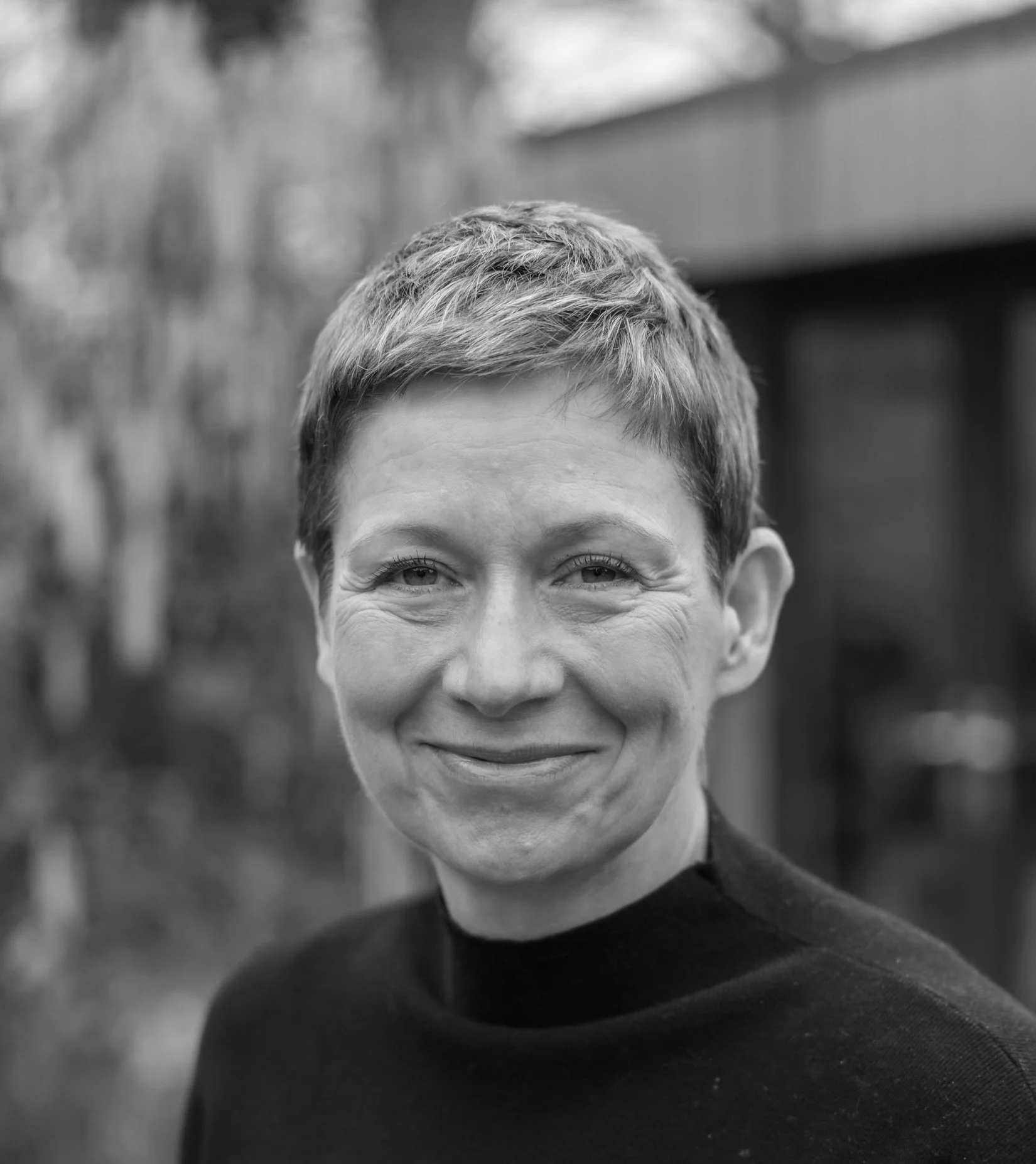 Black and white portrait of a woman with short hair smiling outdoors.
