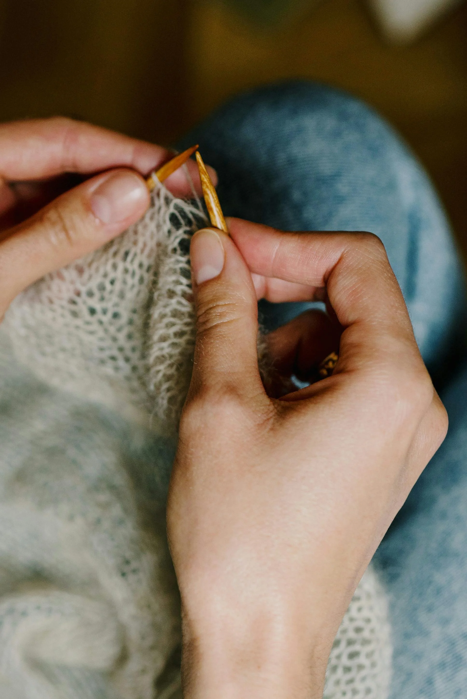 Close-up of hands knitting with wooden needles and cream-colored yarn.
