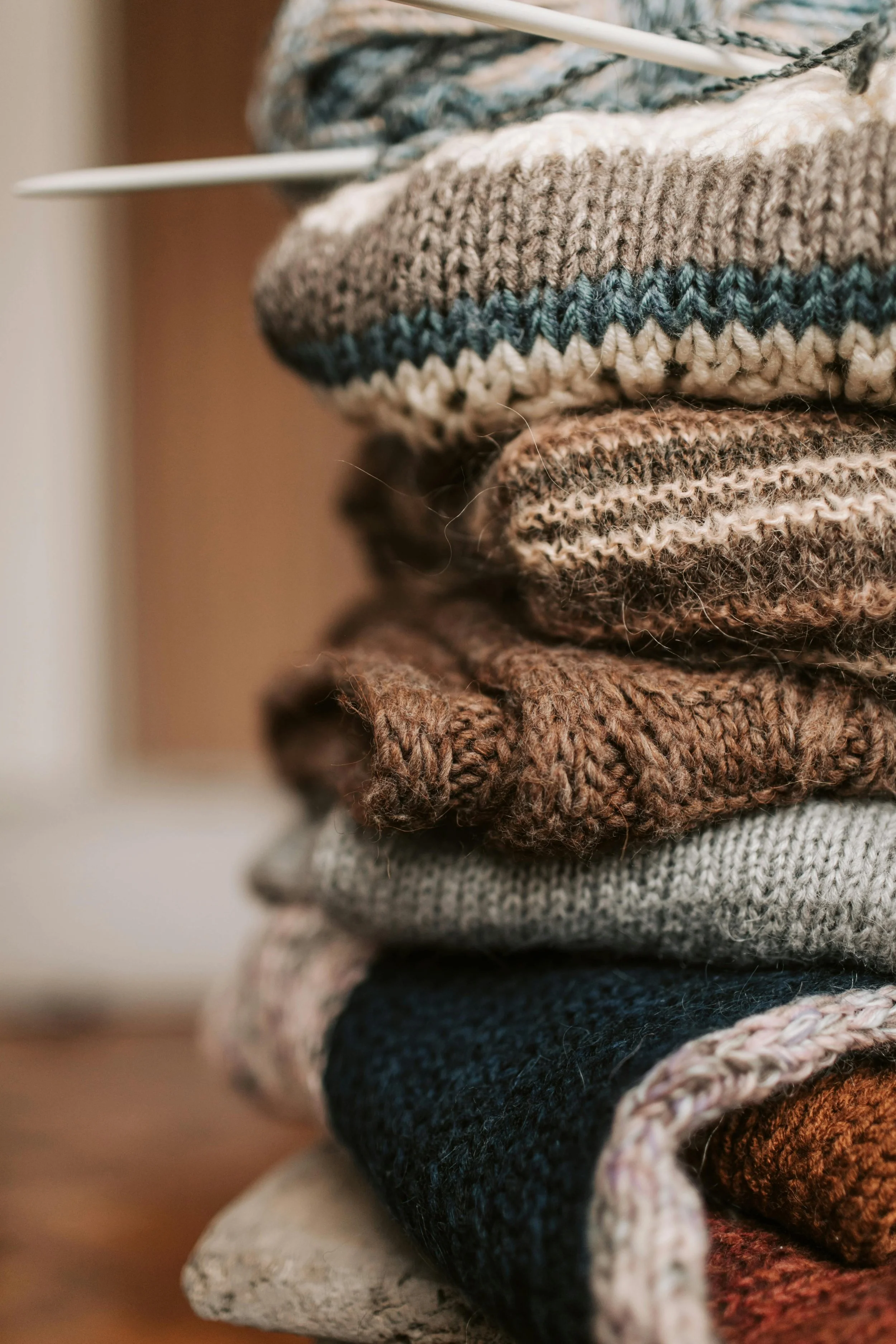 Stack of folded knitted sweaters in various earth tones with different patterns.