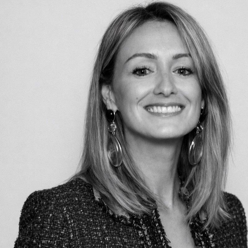Portrait en noir et blanc d'une femme souriante avec des boucle d'oreilles longues et un fait de vêtement sombre.