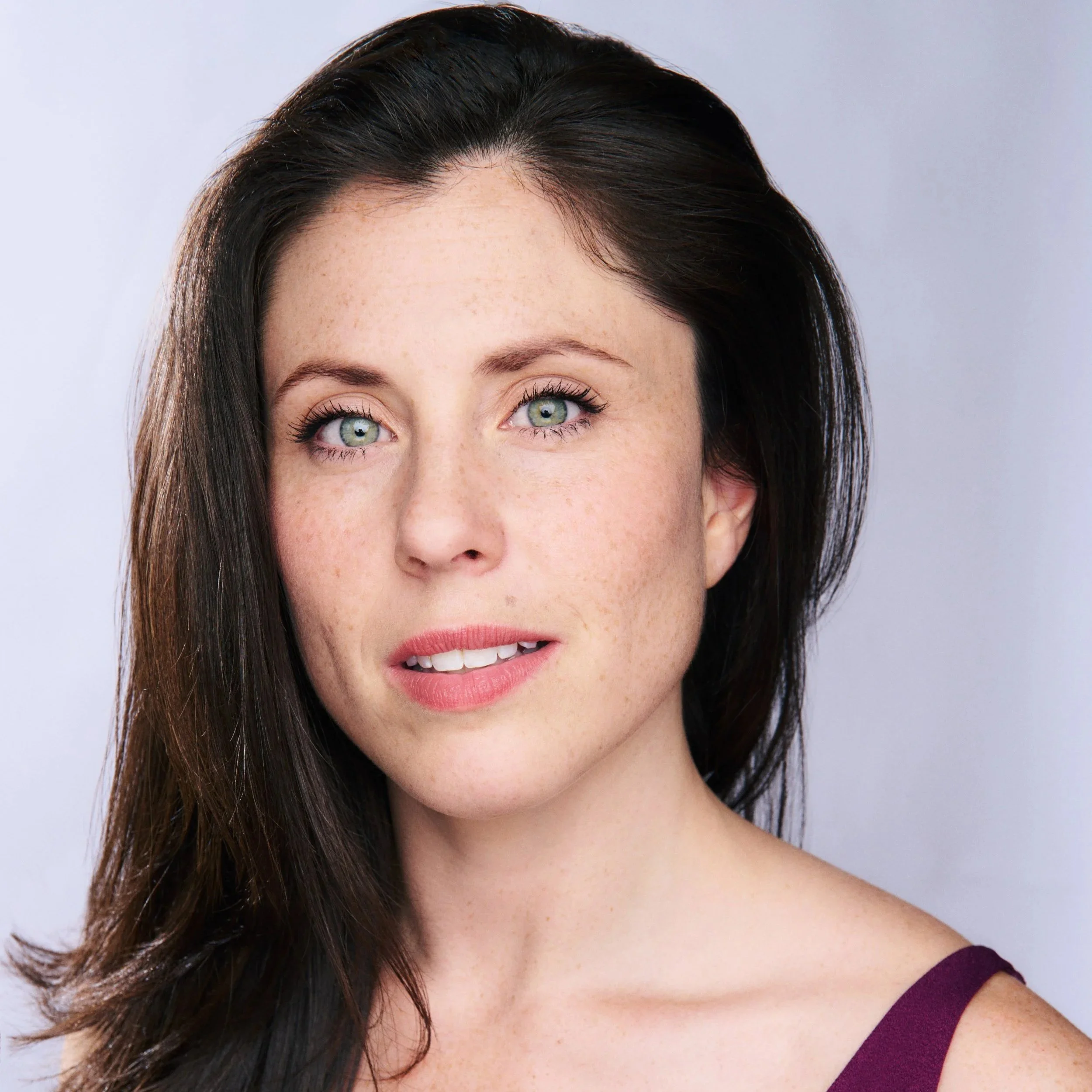 Close-up of a woman with dark hair and blue-green eyes, wearing a purple top.