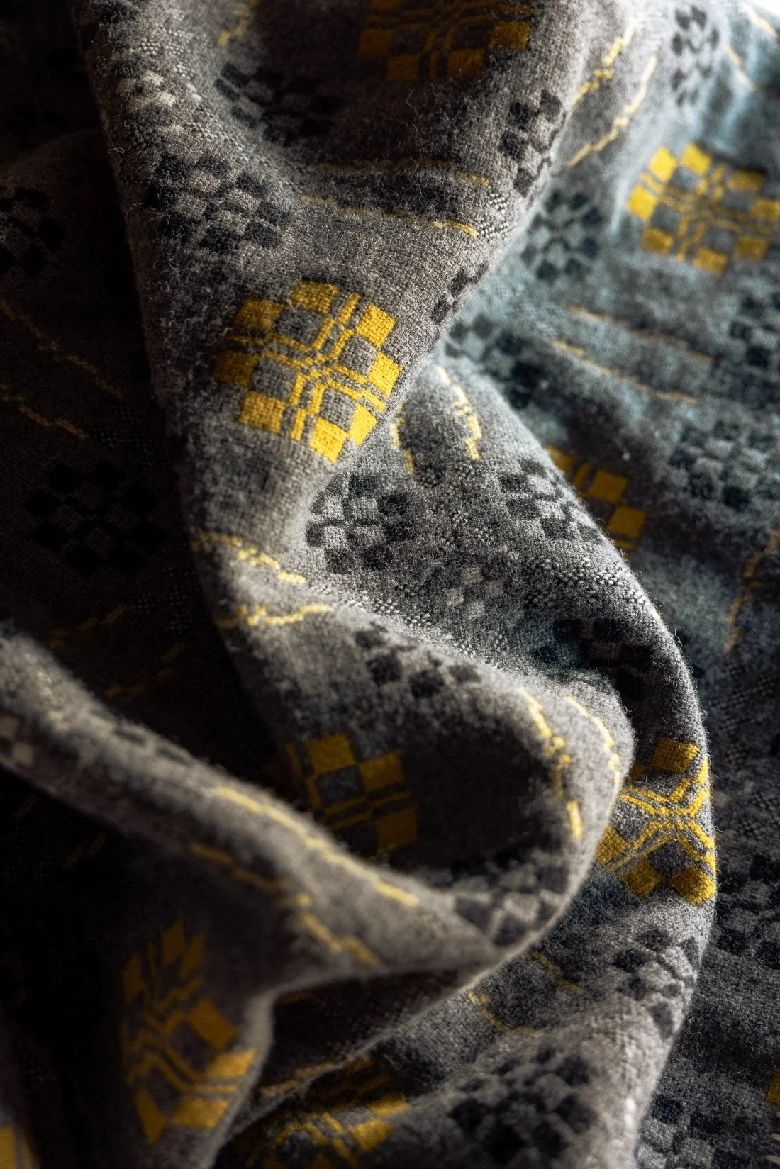 Close-up of a gray fabric with a geometric pattern in black and yellow, showing folds and texture.
