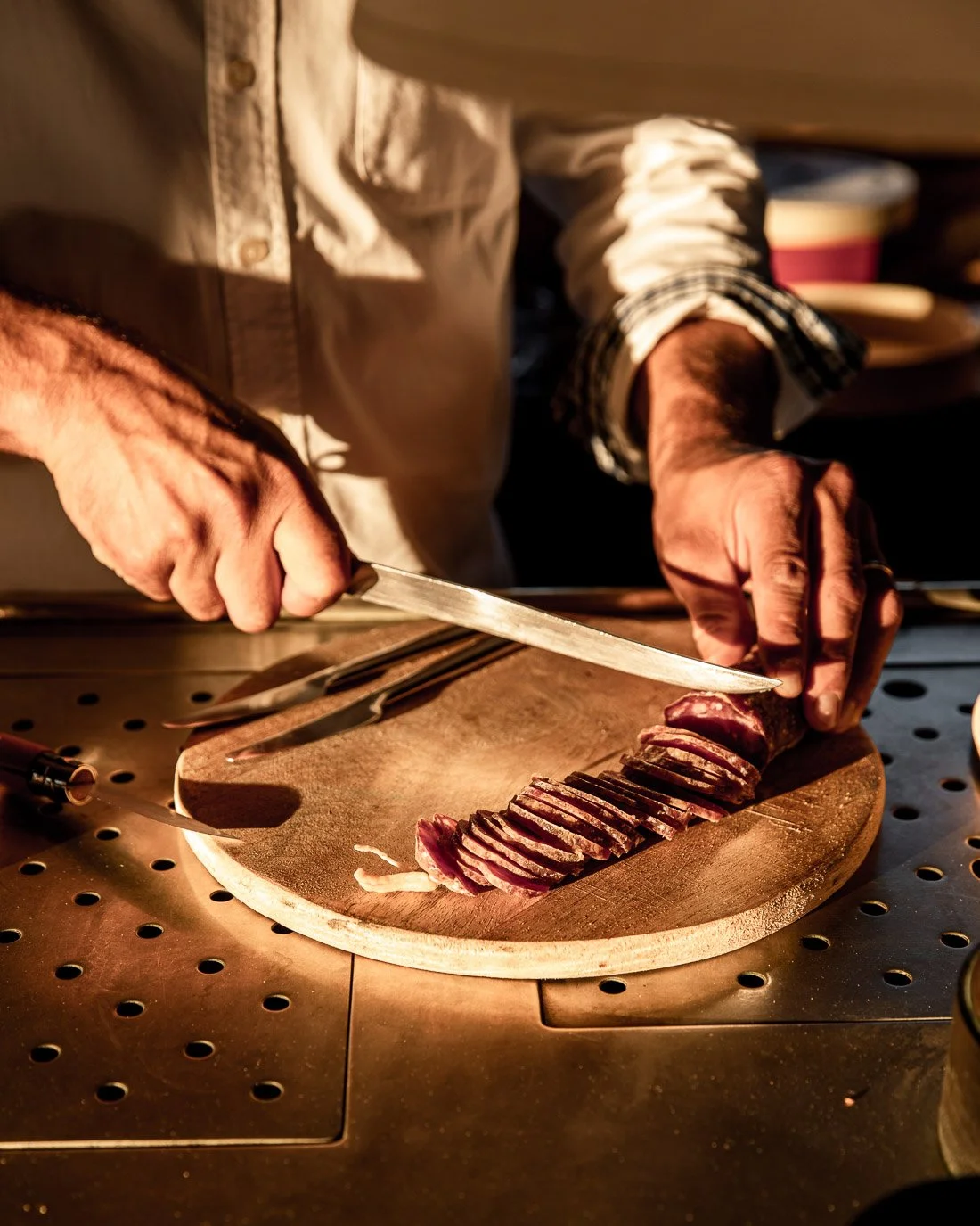 Person slicing cooked meat on a wooden cutting board with a chef's knife in a kitchen setting.