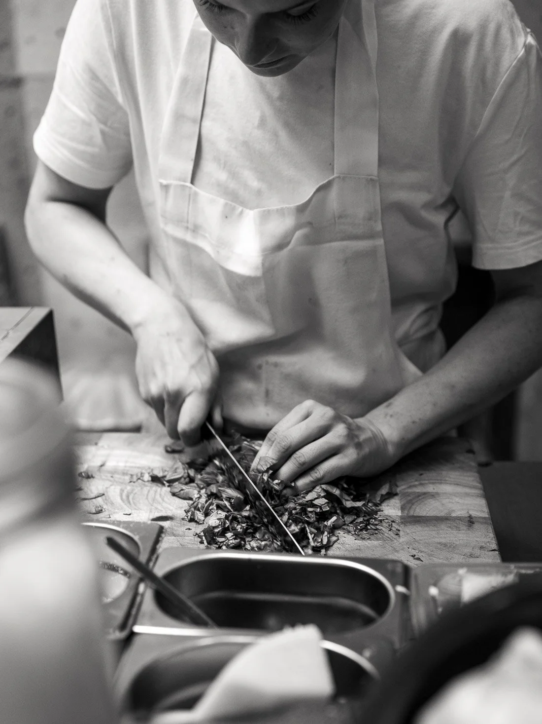 A person cutting vegetables with a knife on a wooden cutting board in a kitchen.
