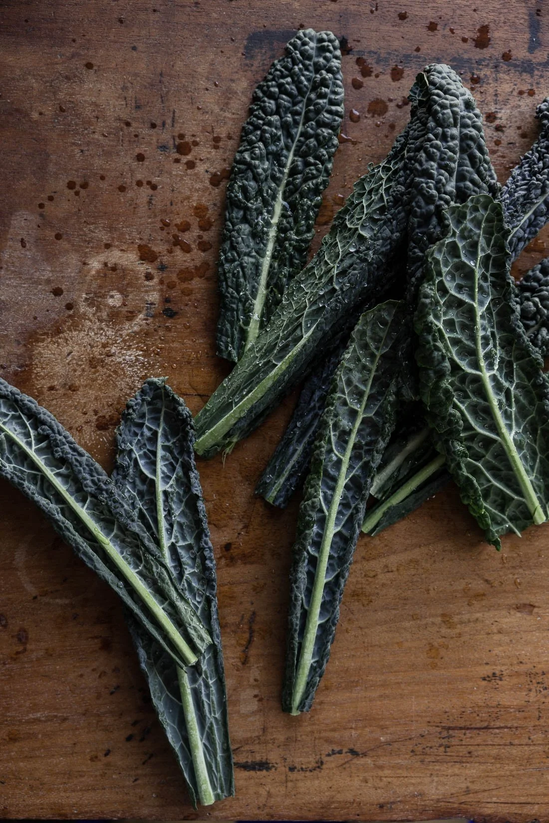 Several dark green kale leaves with water droplets on a wooden surface.