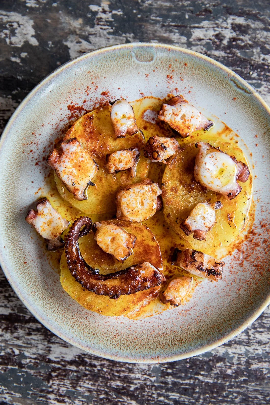 A bowl of grilled octopus served with sliced potatoes and sprinkled with paprika.