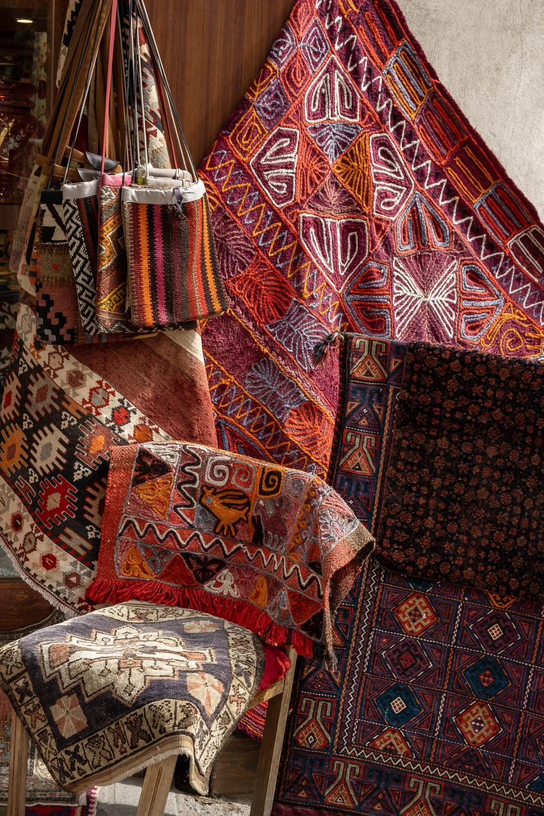 Display of colorful, patterned woven rugs and tapestries hanging and draped on furniture.