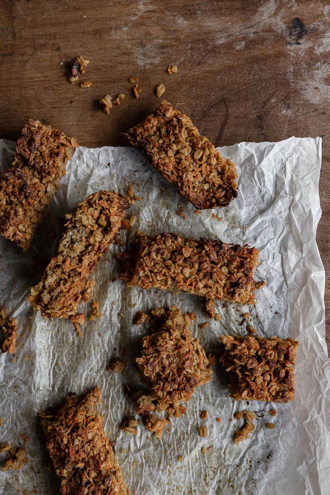 Overhead view of multiple rectangular granola bars on crumpled parchment paper on a wooden surface.