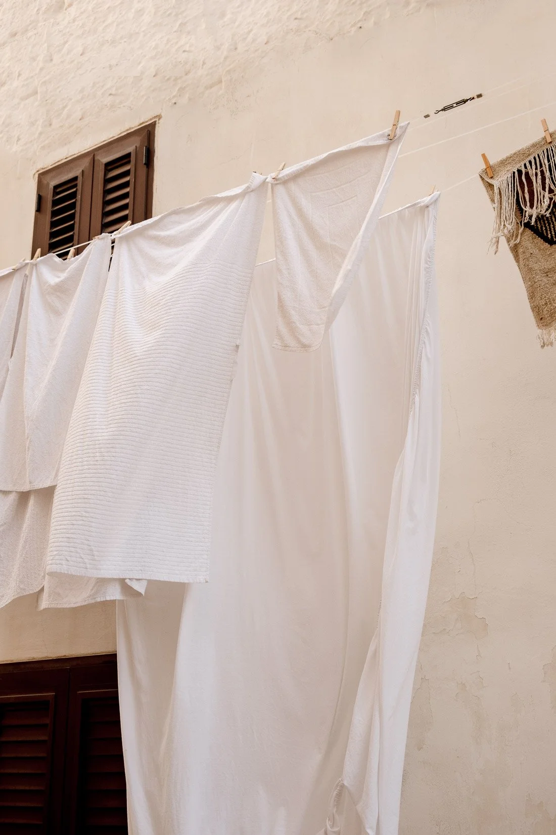 Clothesline with white laundry hanging outside over a beige wall