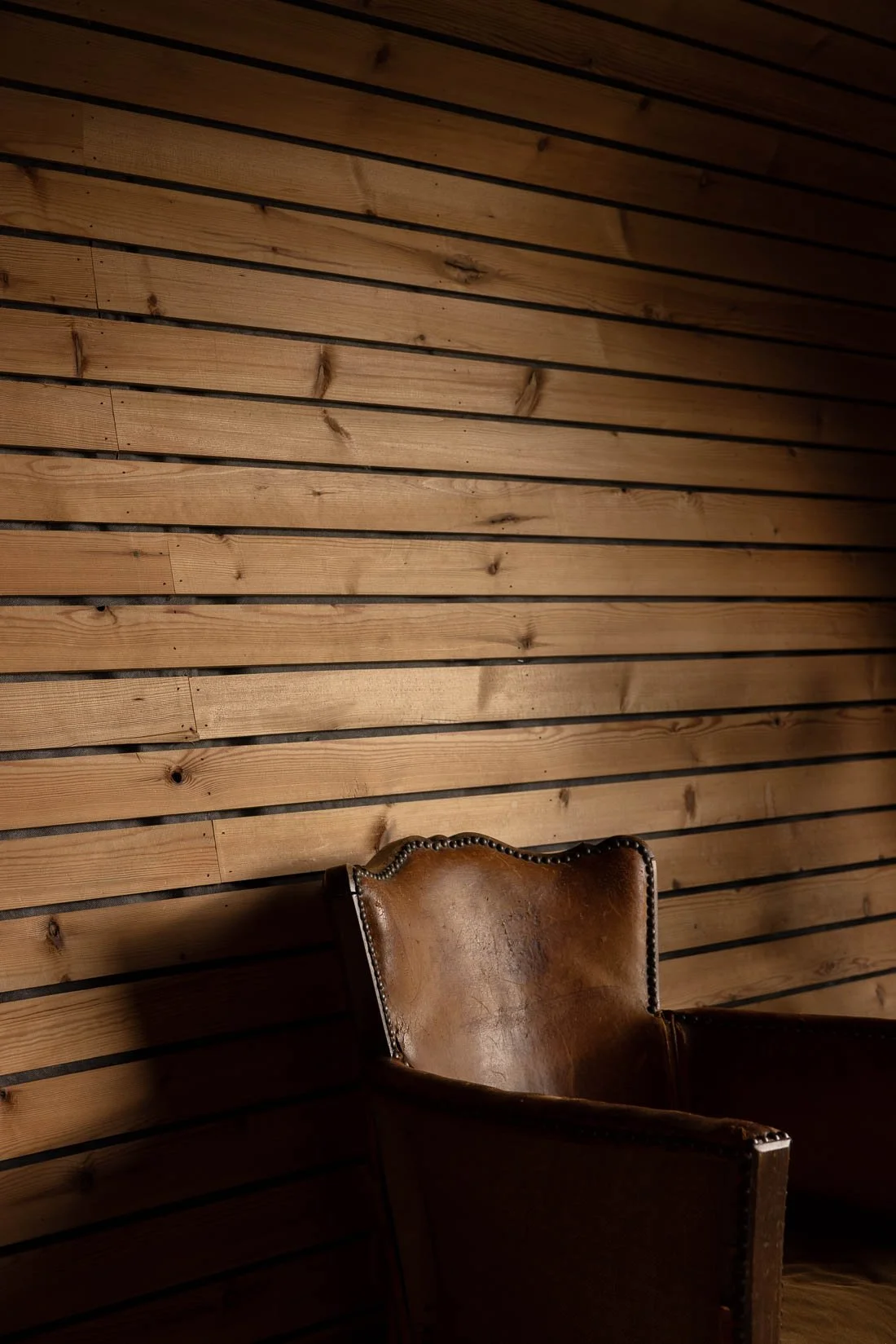 A corner of a room with a leather armchair against a wooden, slatted wall.