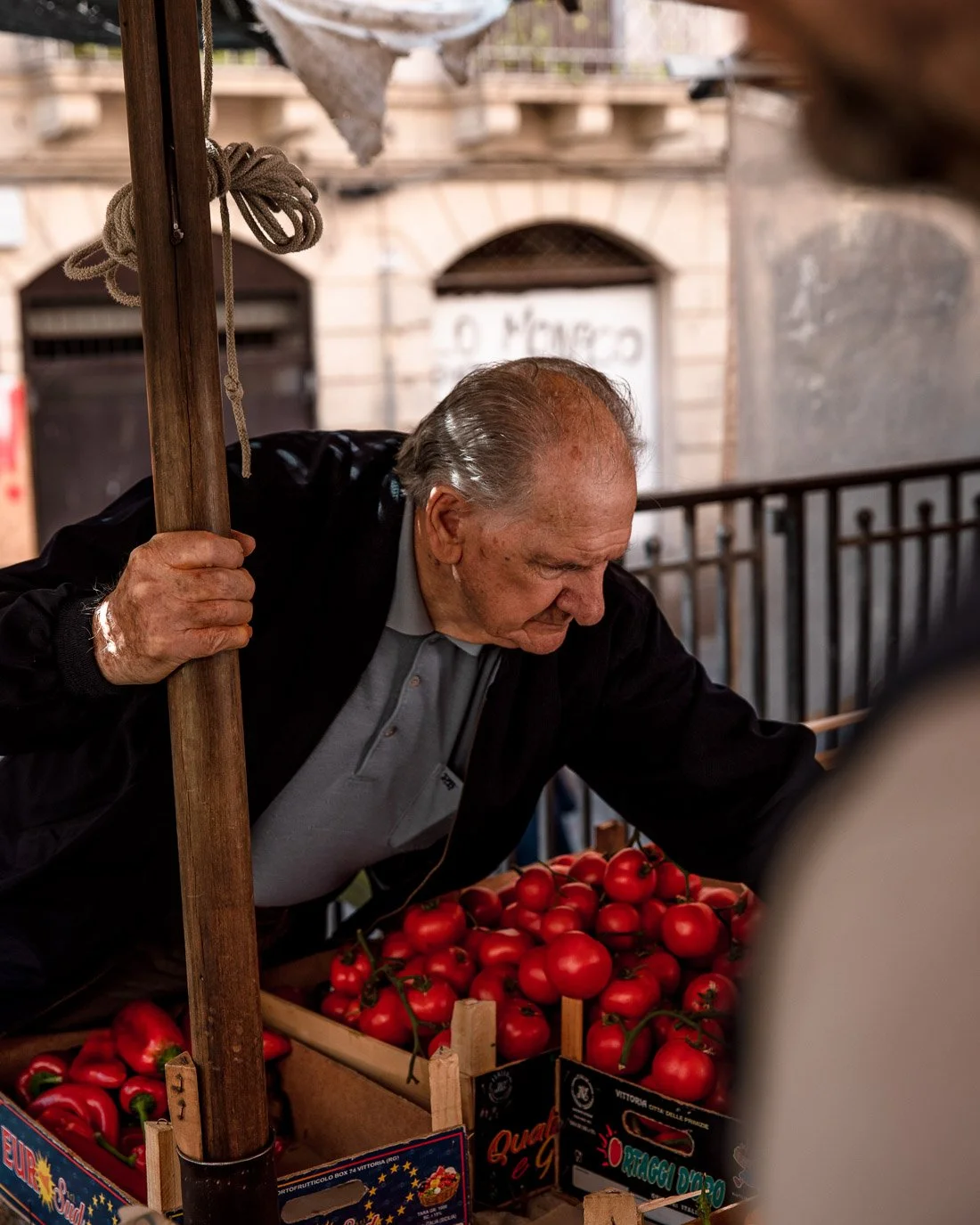 An elderly man selling red tomatoes at an outdoor market stall.