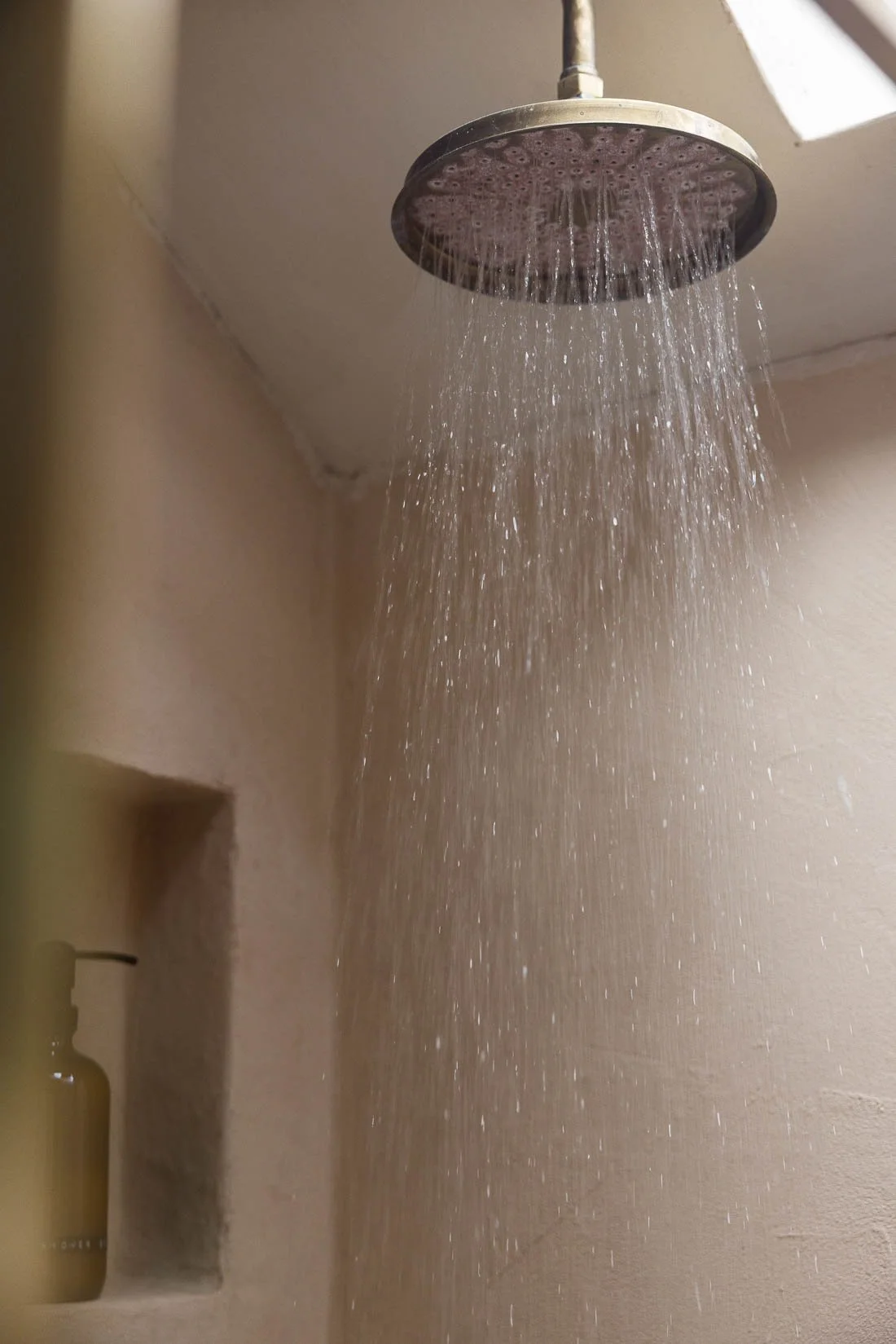 Shower head installed on a bathroom ceiling, water flowing down in multiple streams.