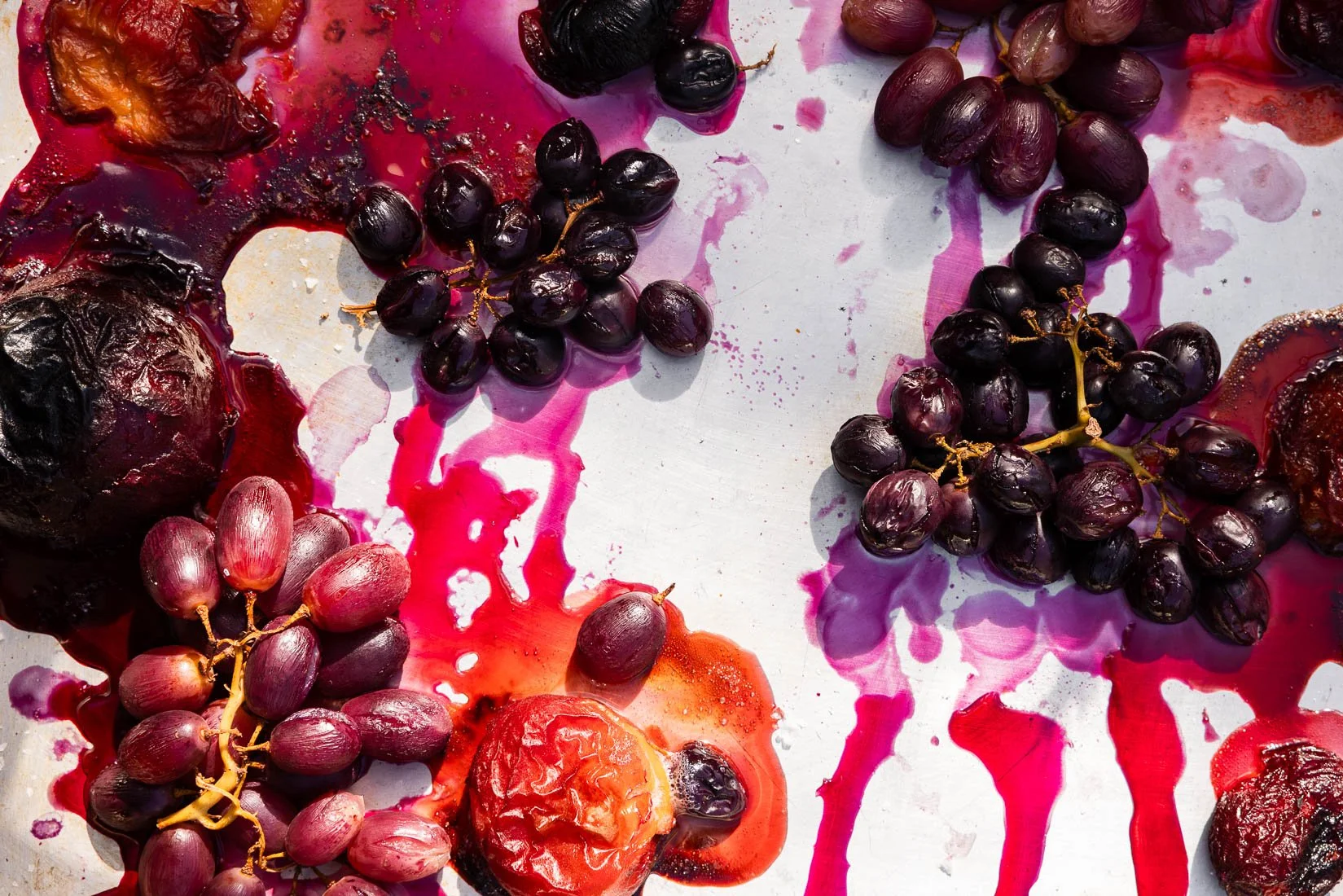 Black and red grapes, some crushed with juice spilled on a white surface.