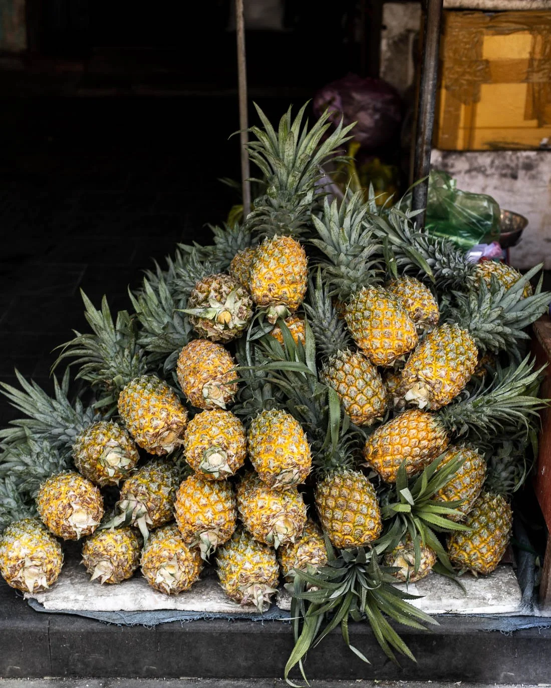 Heap of pineapples with green leaves, displayed on a surface in a market or shop setting.