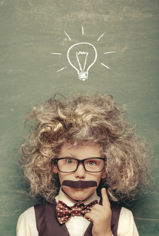 Child dressed as a scientist with curly wig and chalkboard lightbulb drawing, symbolizing big ideas and creative learning.