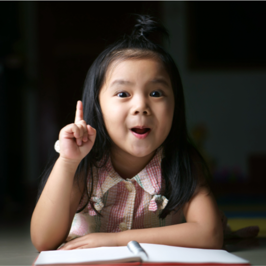 Young girl raising her hand at a desk, showing curiosity and engagement in learning.