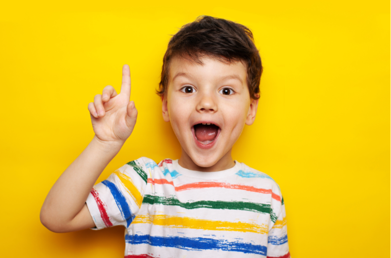 Excited young boy pointing upward against a yellow background, expressing a big idea.