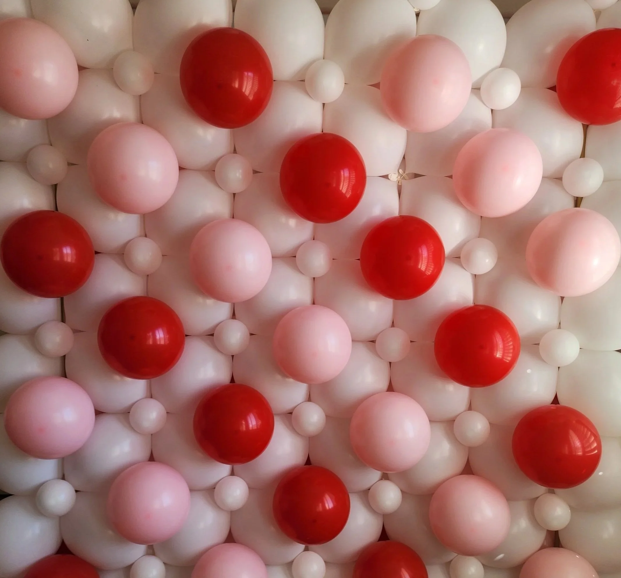 A decorative wall made of white, pink, and red plastic balls arranged in a pattern.