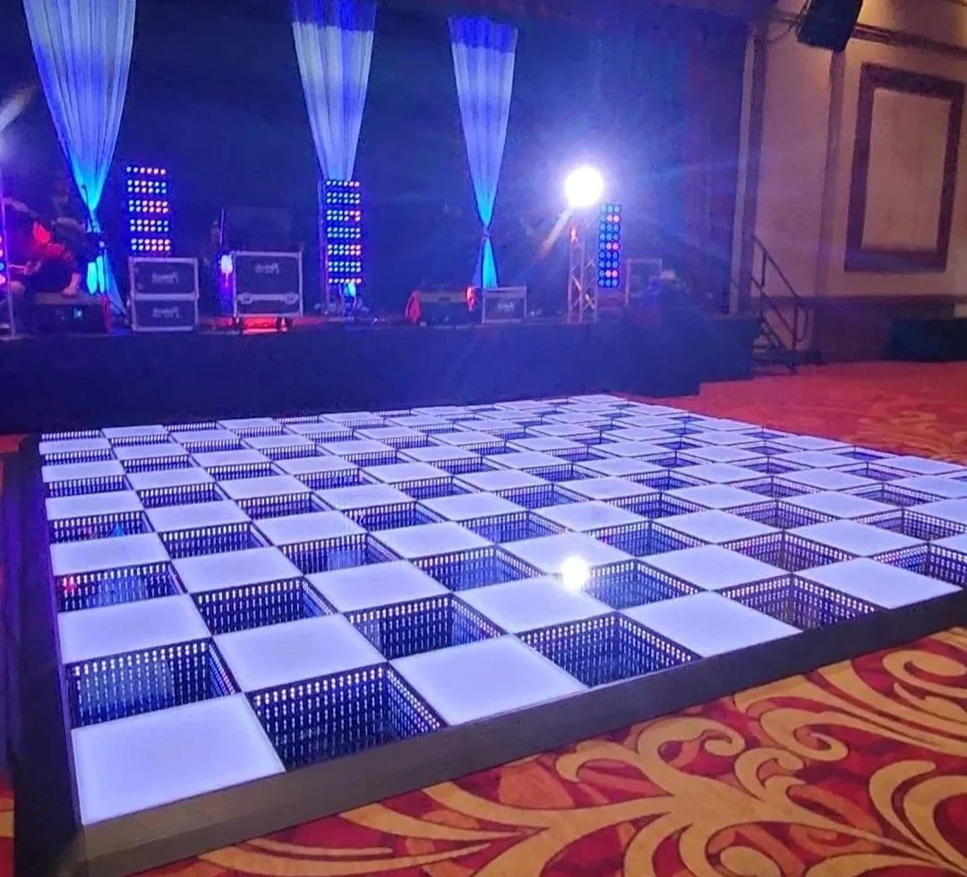 A dance floor with illuminated square tiles and a stage with lighting and sound equipment in the background.