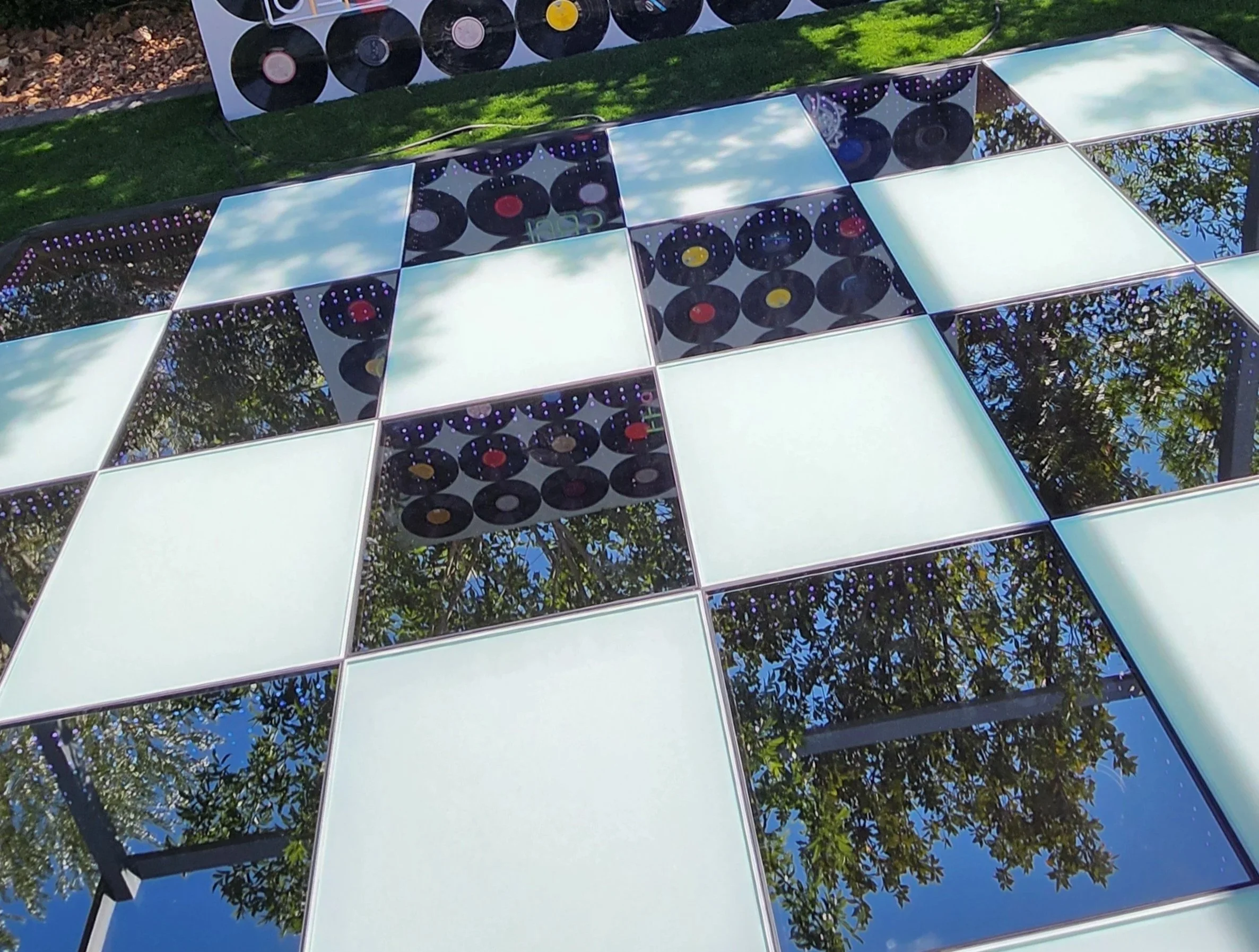 Modern outdoor installation with large reflective mirrors and LED panels arranged in a grid, reflecting trees and the sky.