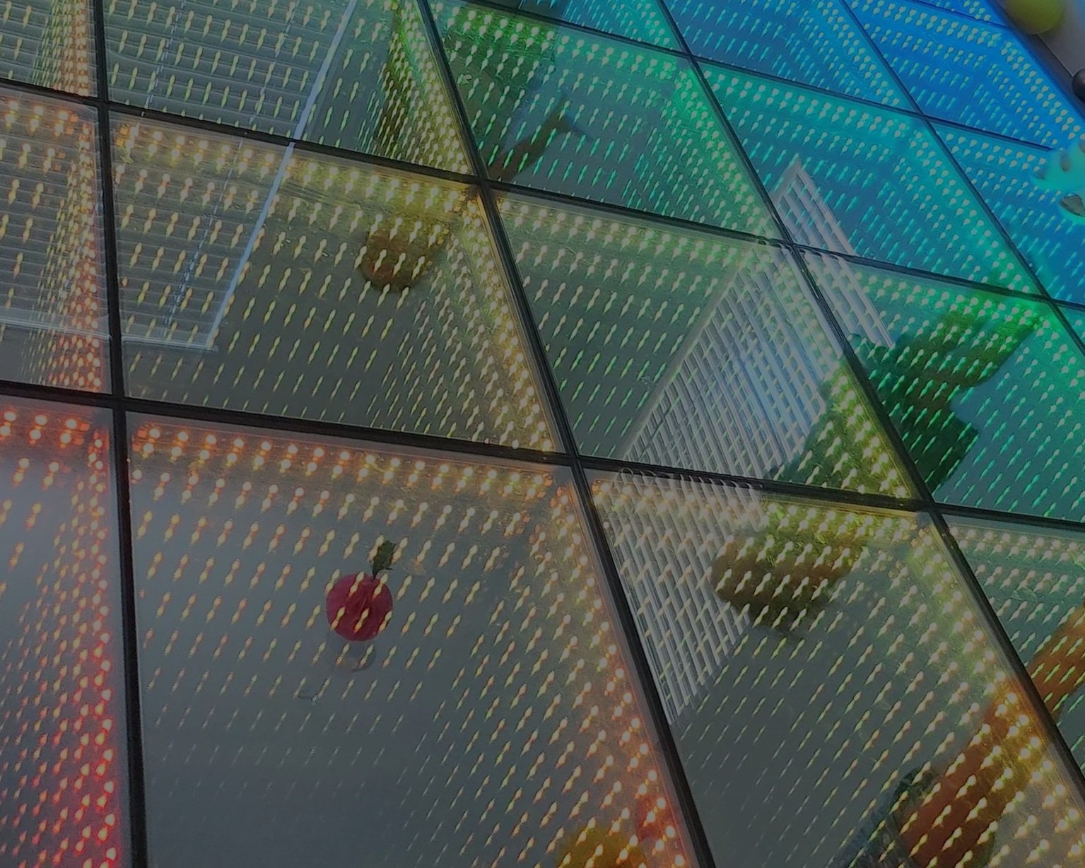 Colorful glass panels with reflections, including buildings, red balloons, and street lights.