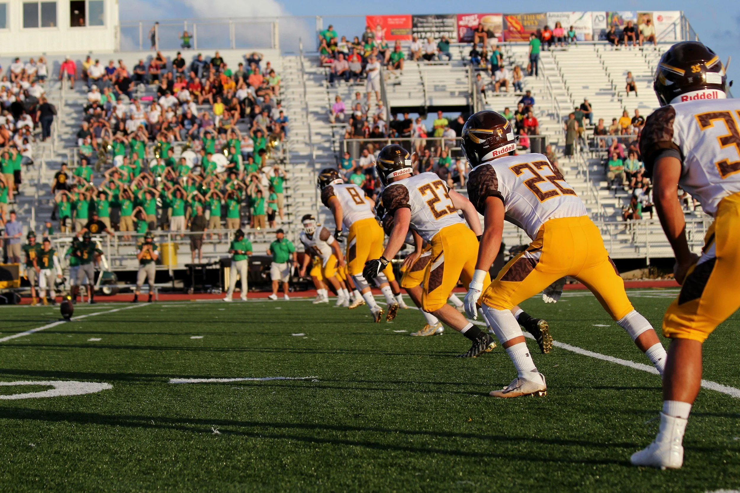 American football players in formation on the field during a game, with spectators in the stands watching.
