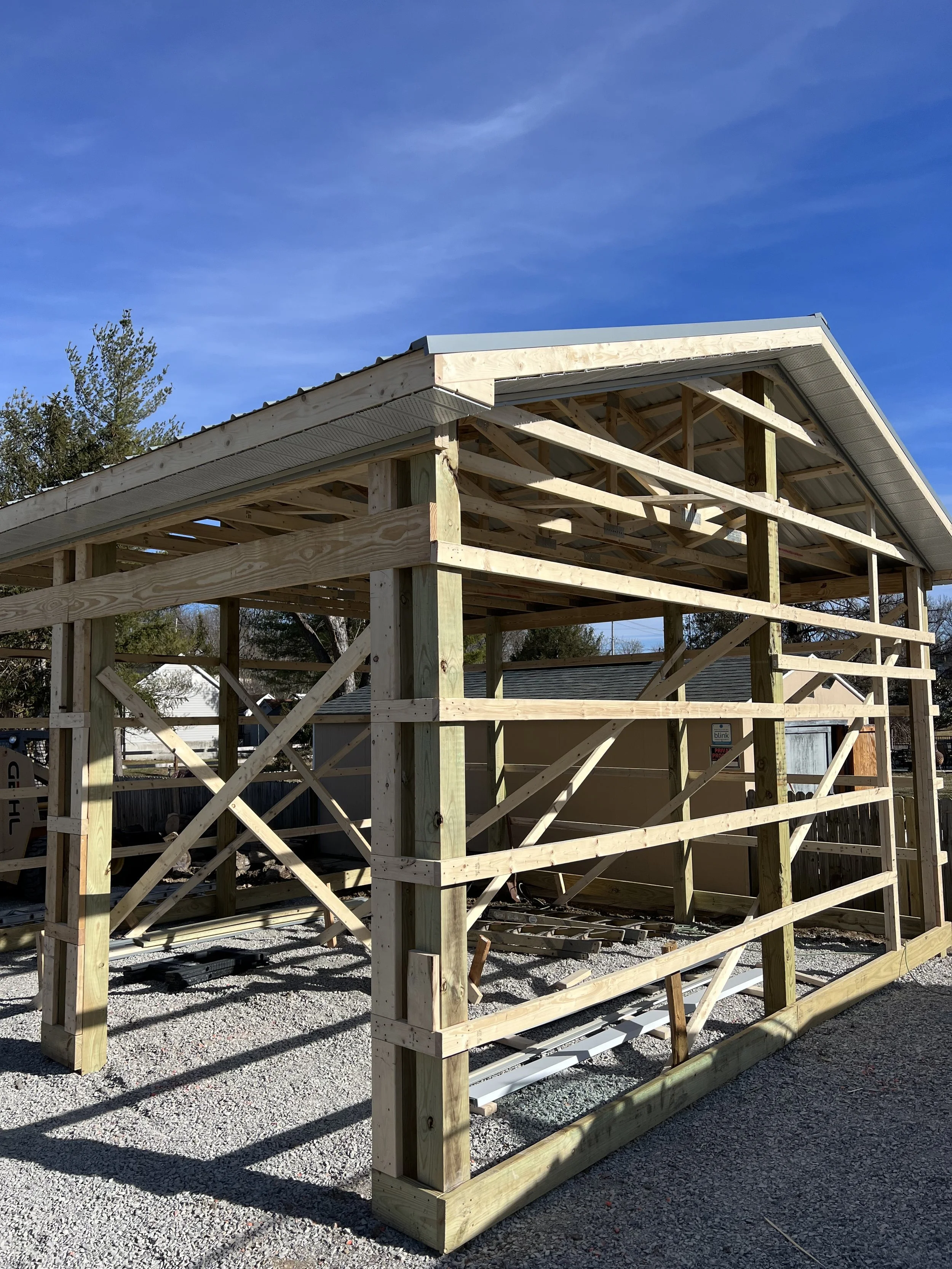 Wooden house under construction with framing and roof structure in progress, set against a blue sky.