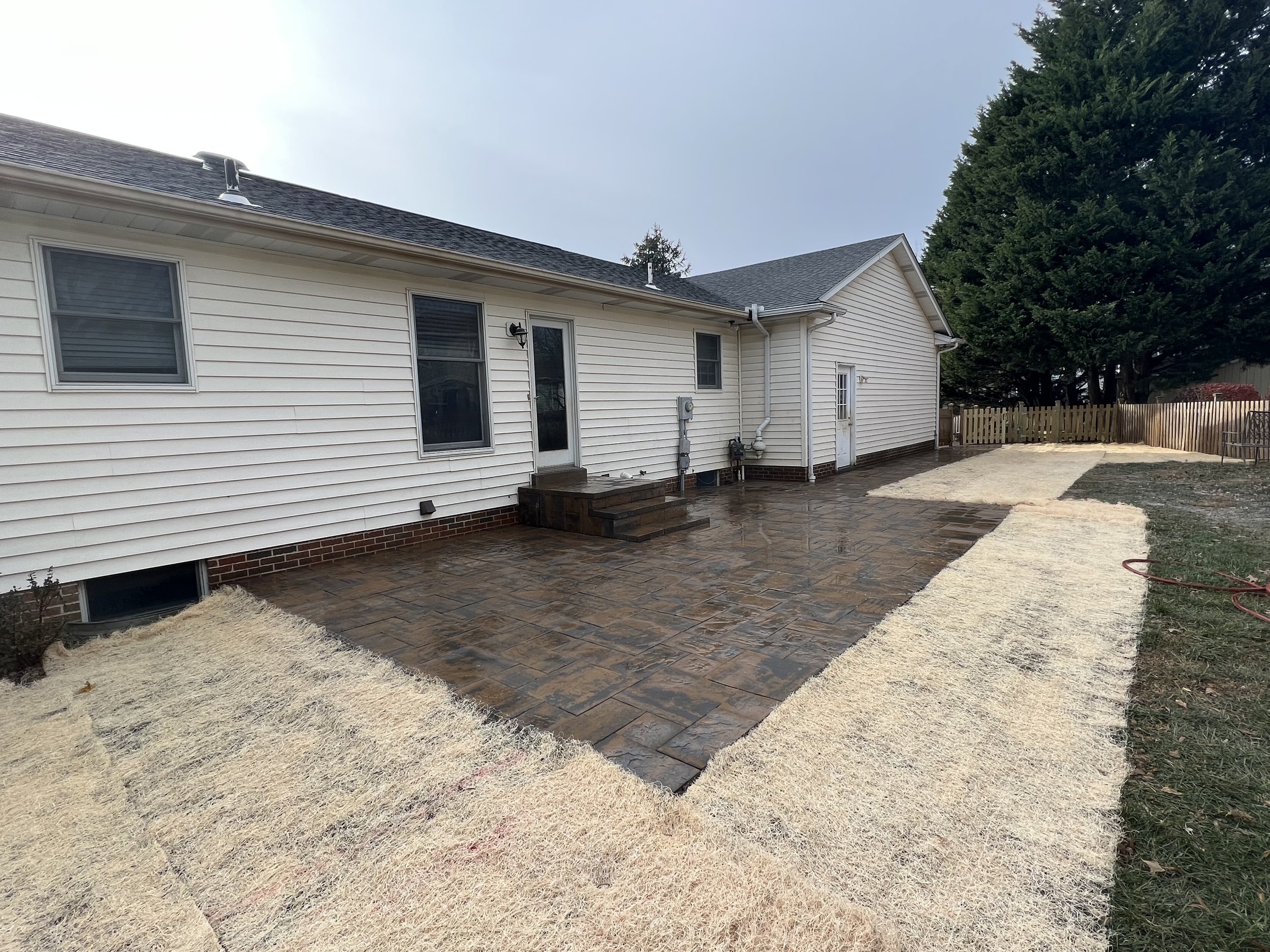Backyard patio with newly installed stone pavers and a fenced yard with trees.