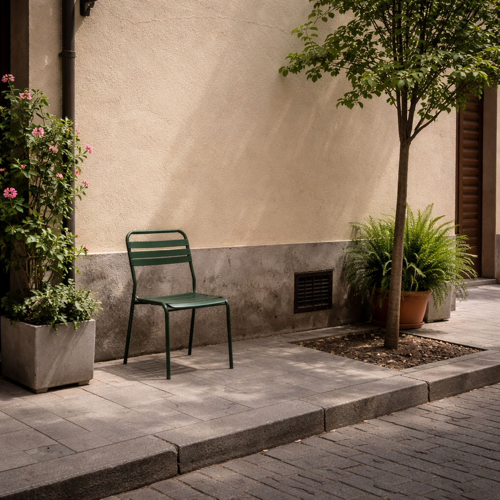 Small urban corner in Madrid in spring with a pale wall, pavement, tree, plants and a green metal chair.