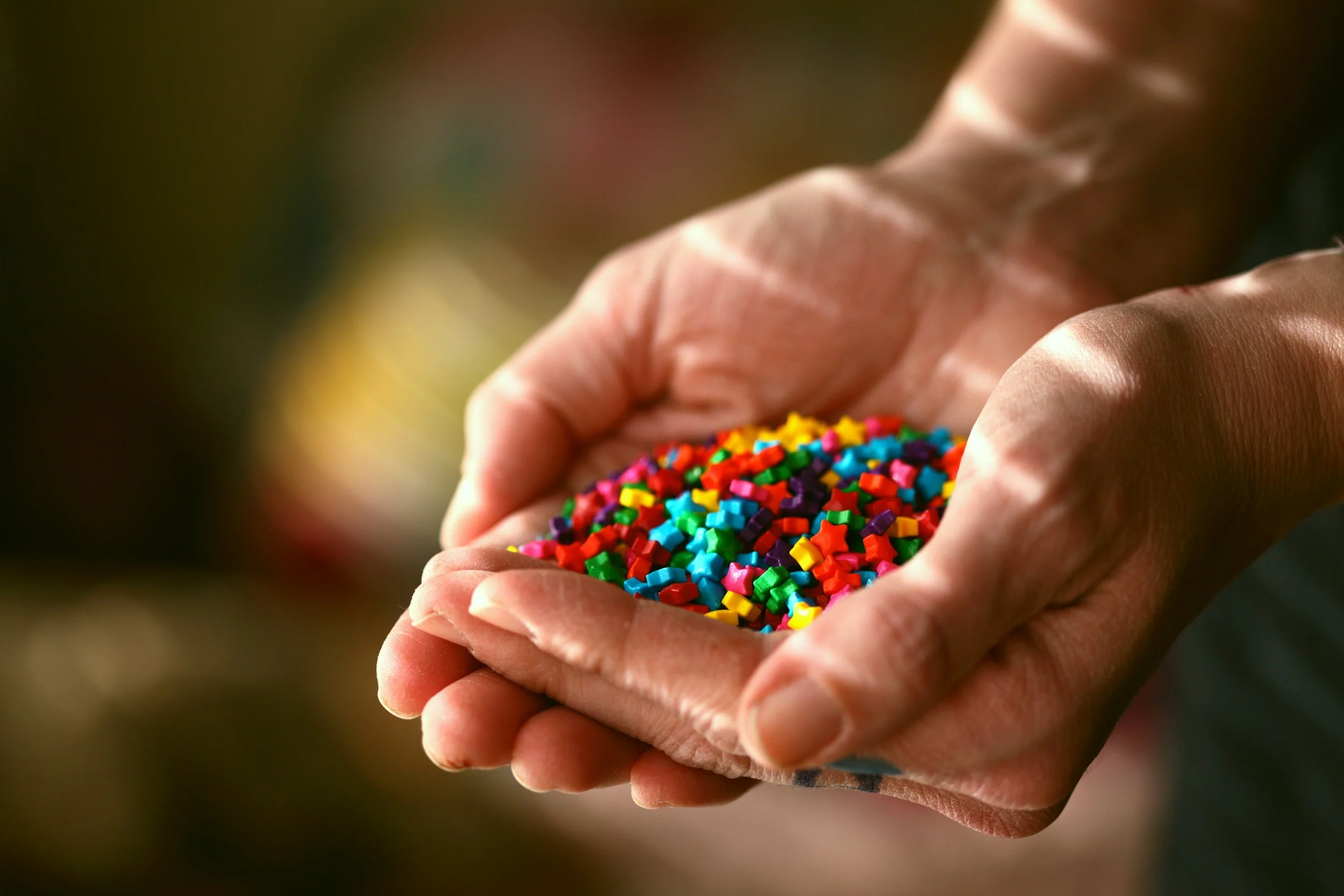 Hands holding a handful of colorful star-shaped sprinkles.