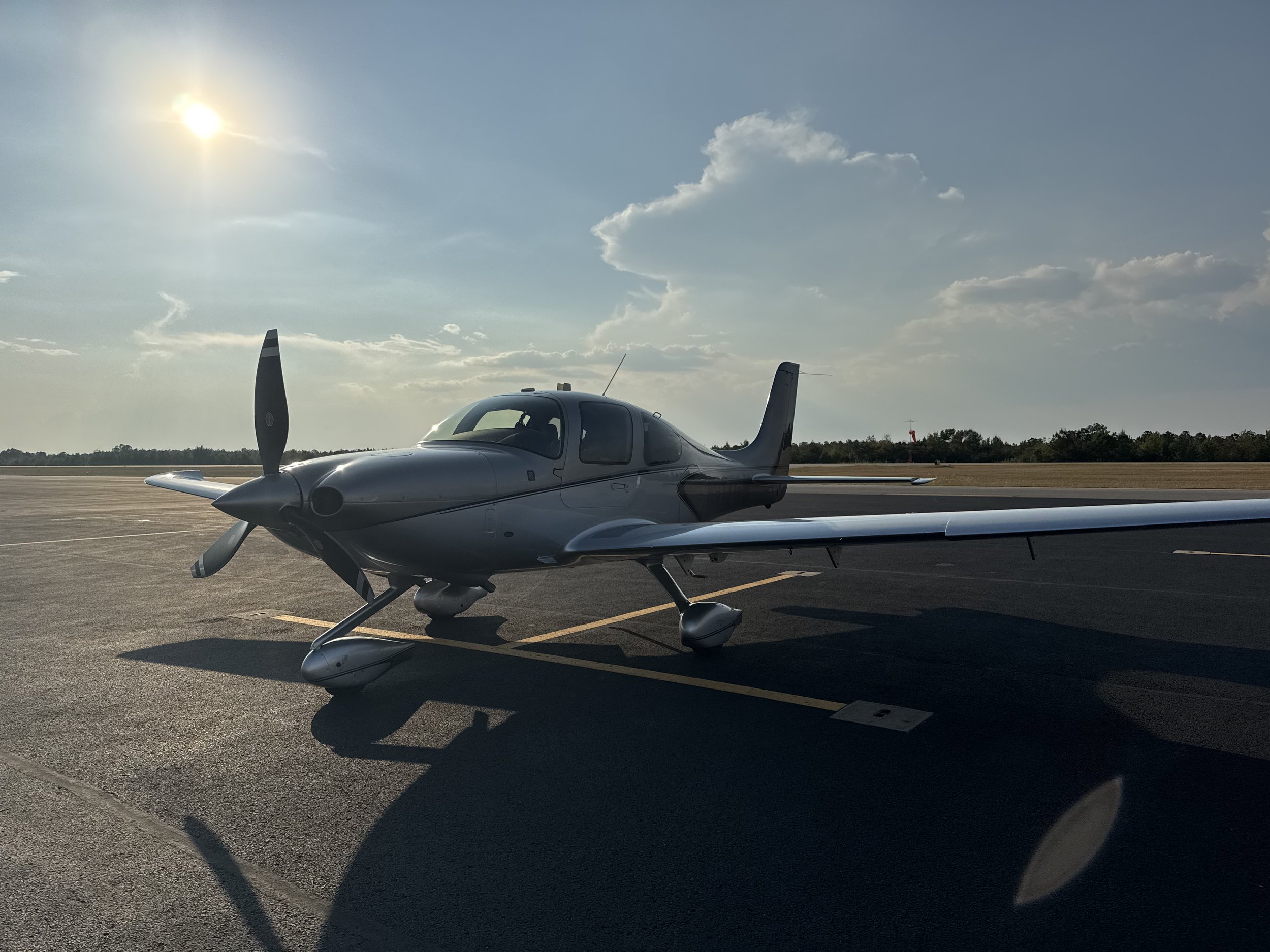 Small modern silver airplane parked on an empty airport tarmac during late afternoon with the sun low in the sky.
