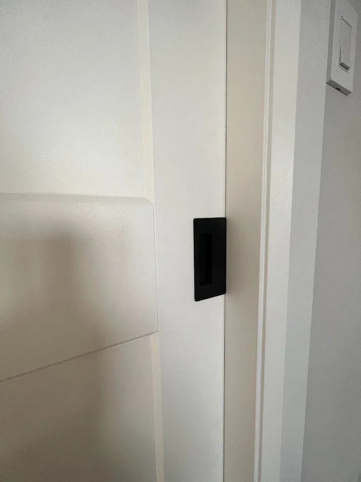 Close-up of a white sliding door with a black handle in a modern interior setting.