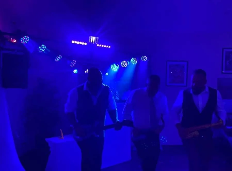 Three musicians playing guitars in a dimly lit room with colorful stage lights.