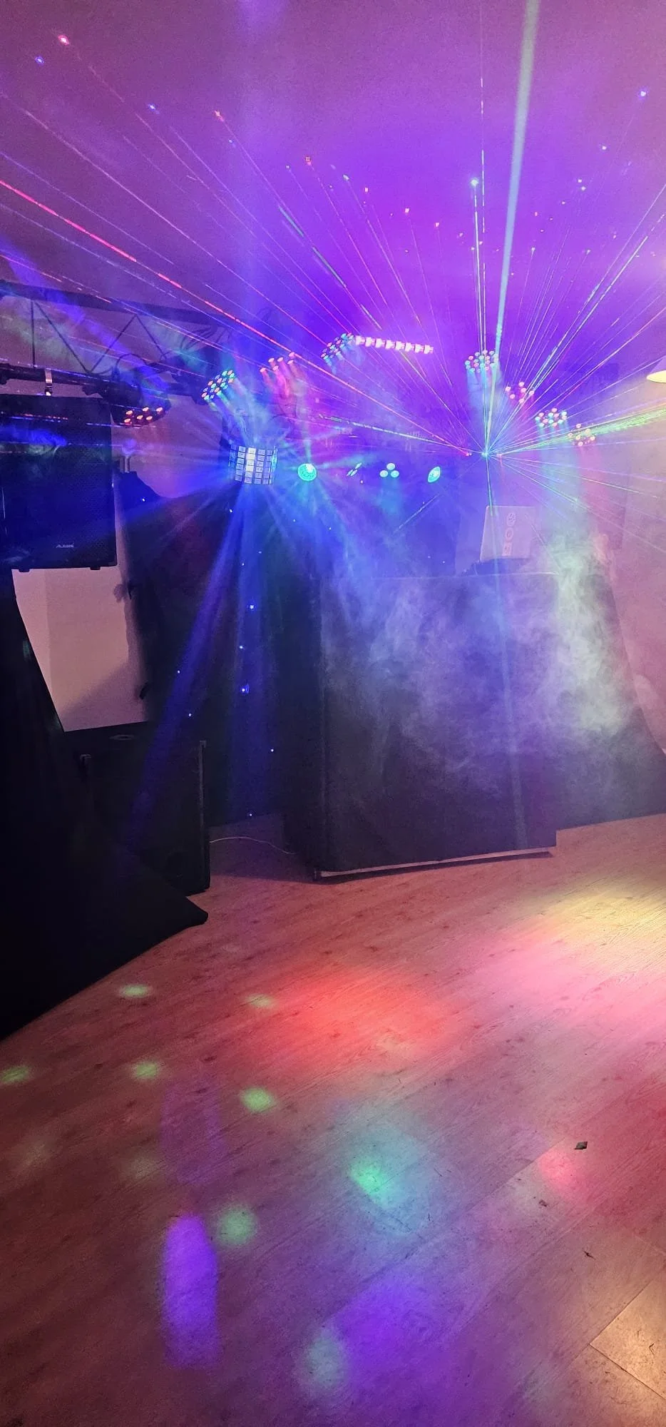 Colorful laser lights and disco ball reflections on a dance floor with speakers and lighting equipment in the background.