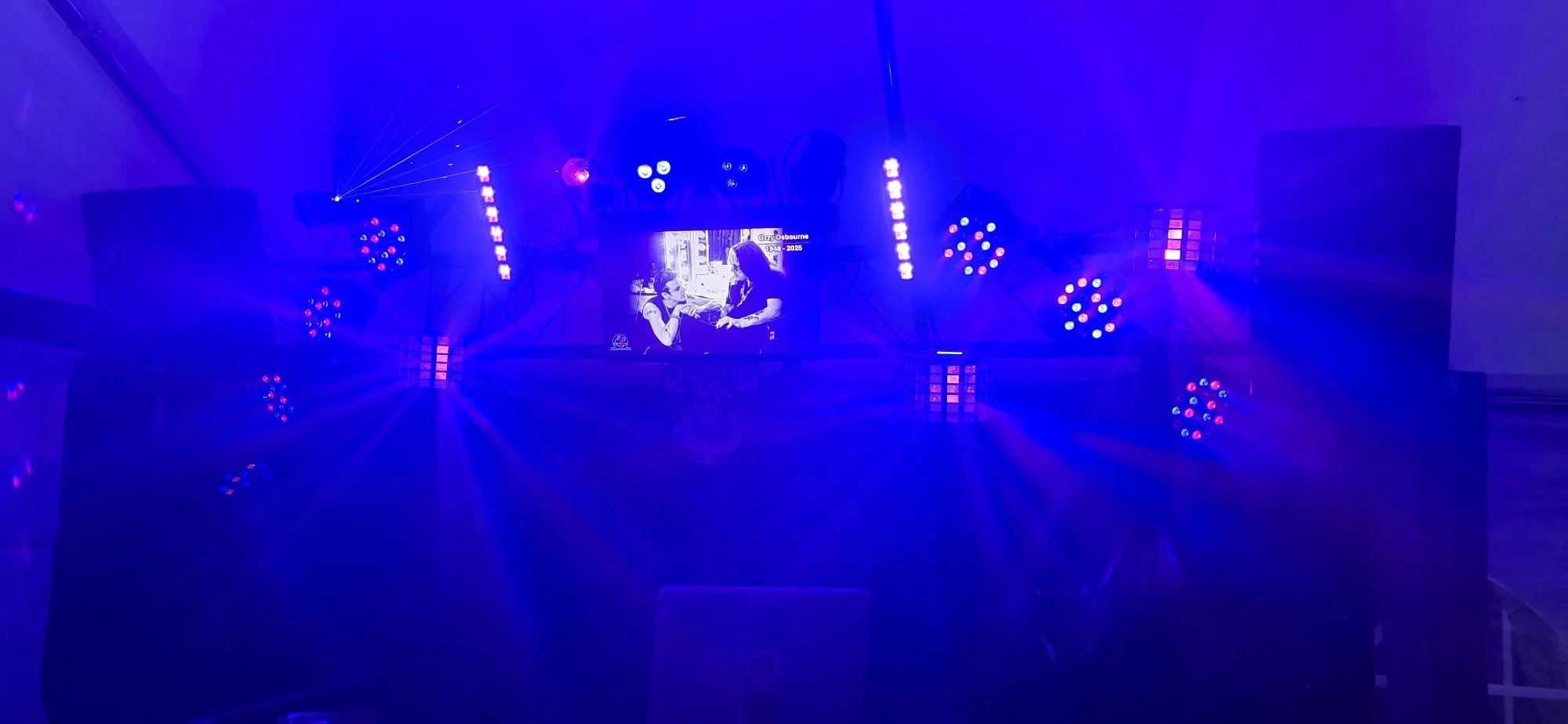 Stage with blue and purple lighting, multiple speakers, and LED lights. A screen displays two women in conversation.