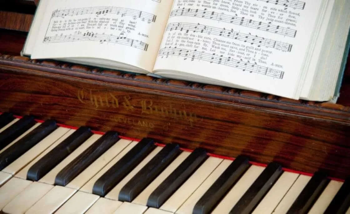 Close-up of a wooden piano with sheet music and a book on top of the keyboard.