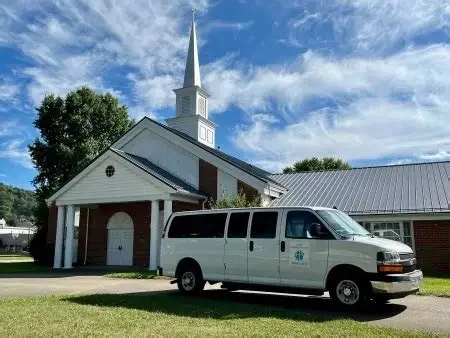 White church with steeple and a van parked in front