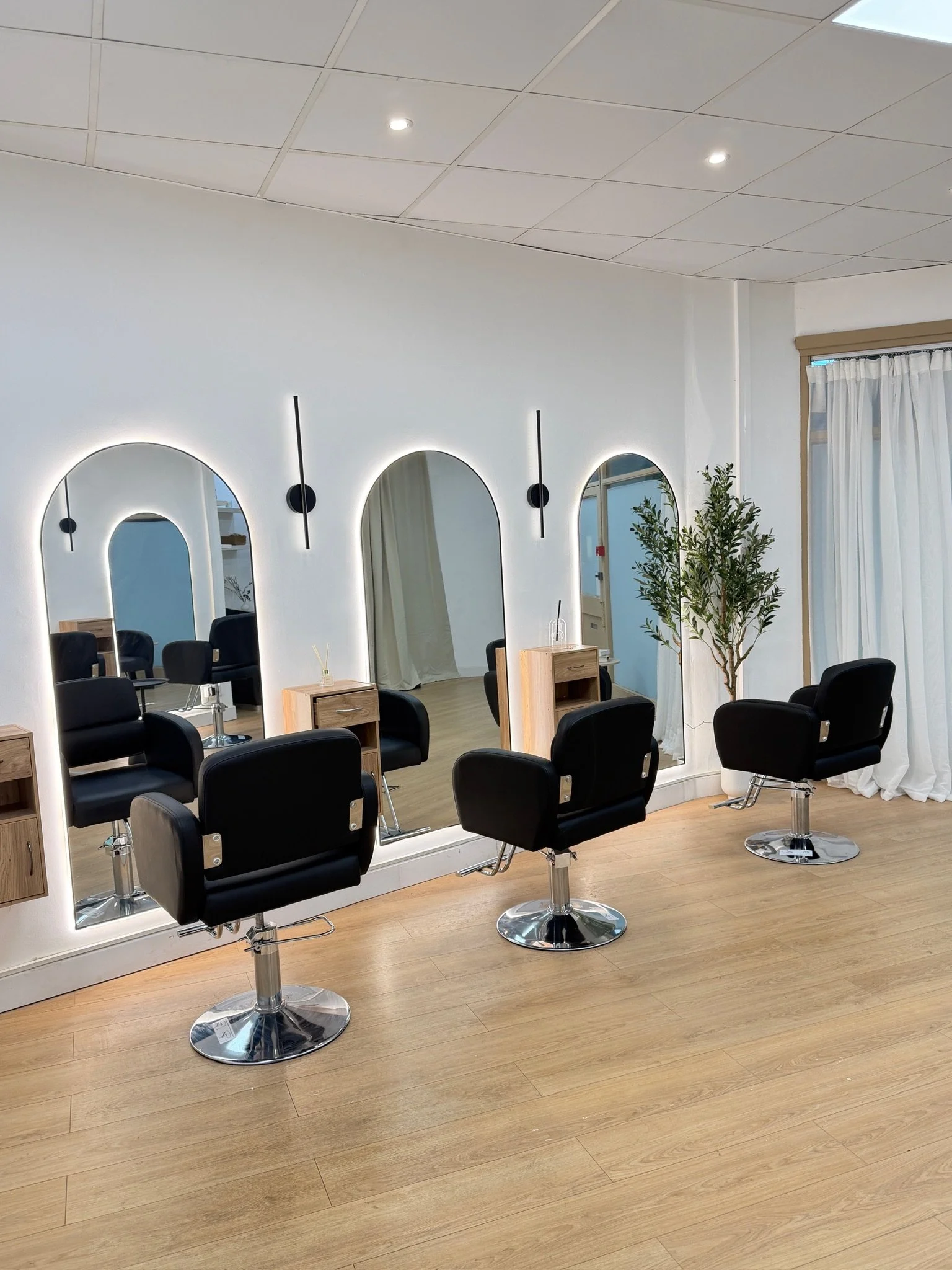 Bright salon interior with black styling chairs, large mirrors and wooden cabinets at AMIA