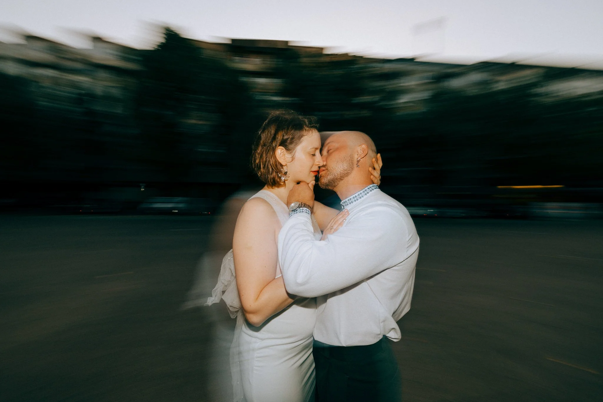 A couple is embracing and about to kiss outdoors at dusk.