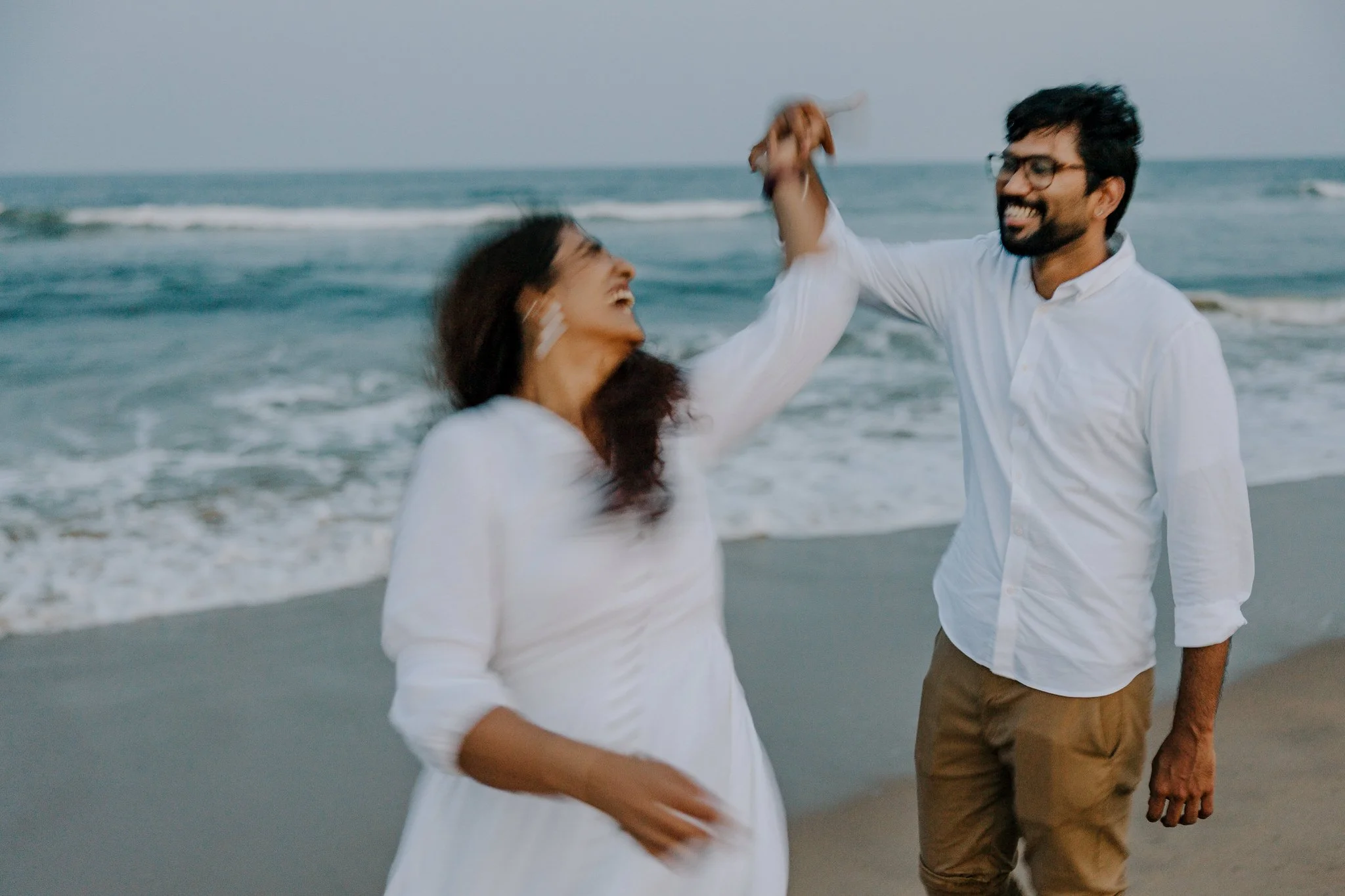 A man and woman enjoying a dance on the beach, with the ocean waves in the background.
