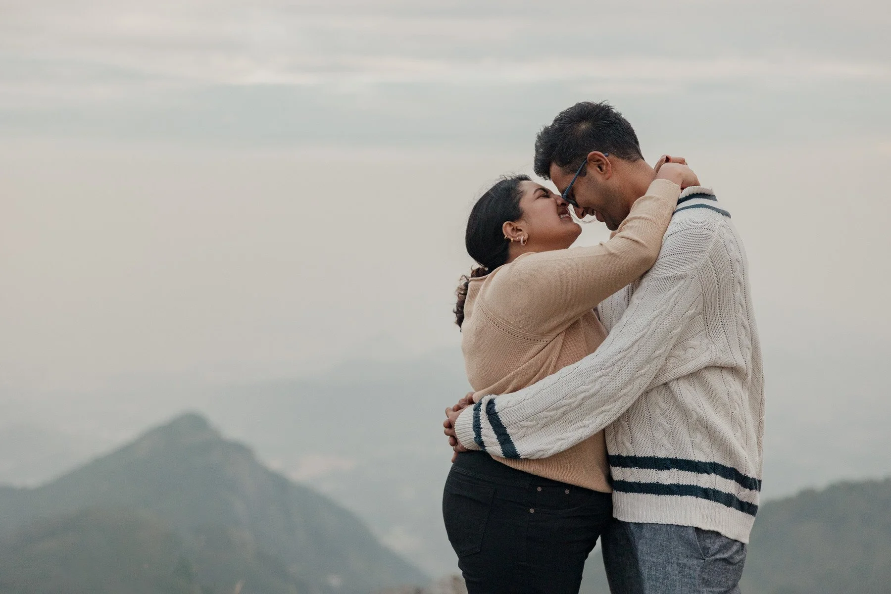 A couple embracing outdoors with mountains in the background.