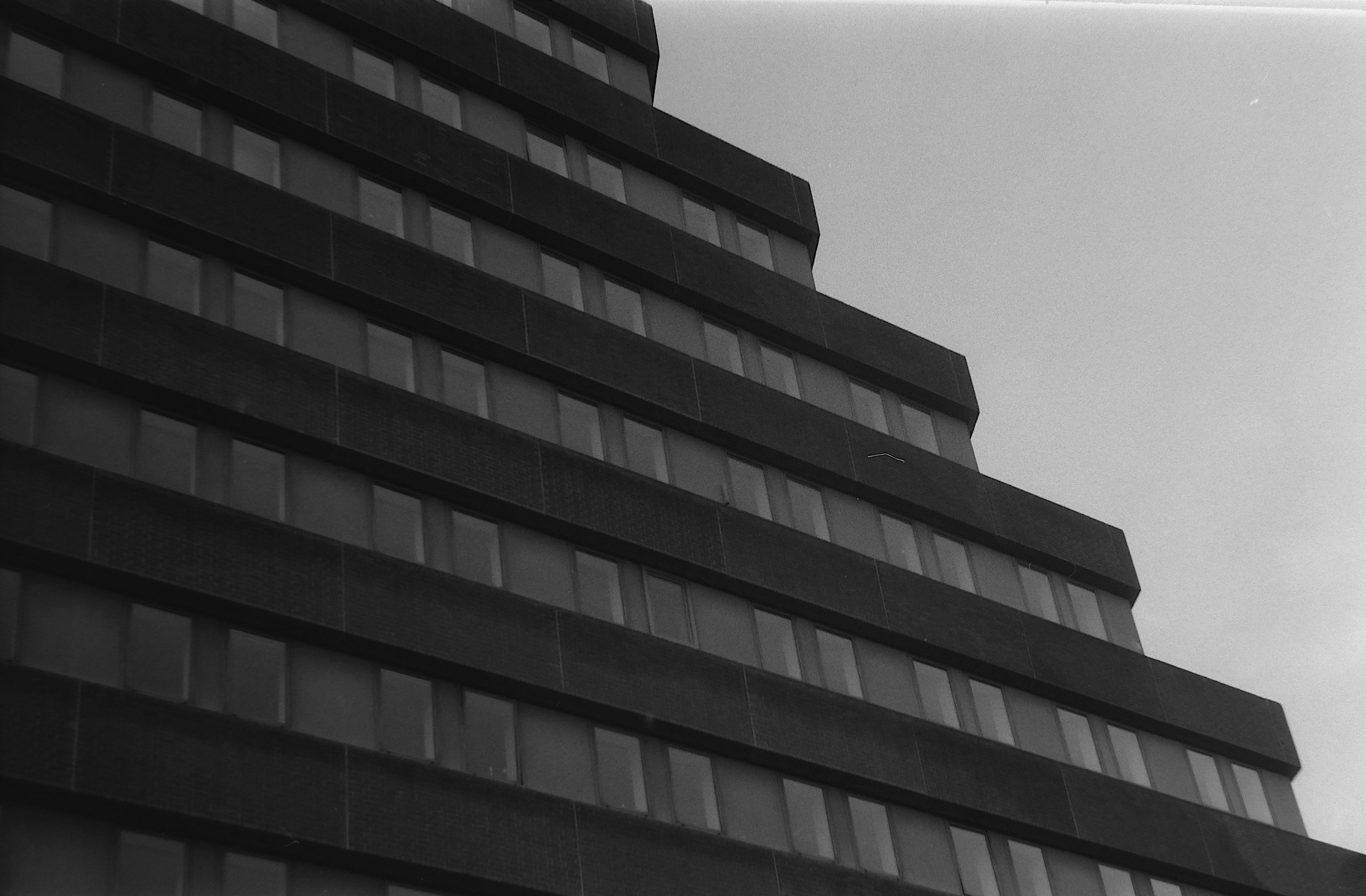 A tall high-rise building with multiple floors, featuring large rectangular windows, against an overcast sky.